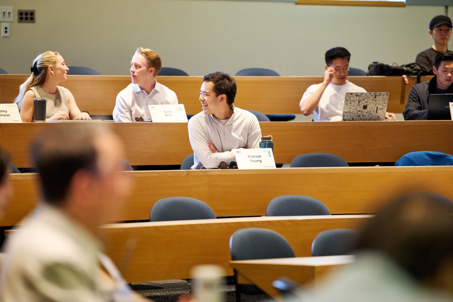 Half a dozen students conversing in a lecture hall. Patrick Yeung is smiling at someone off-camera