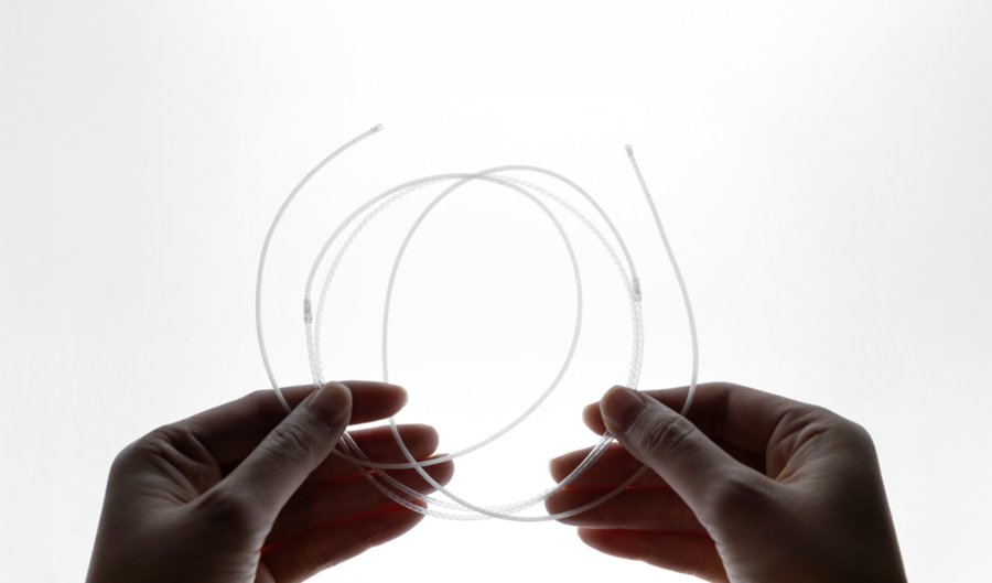 Two hands holding a coil of thin, transparent fiber tubing