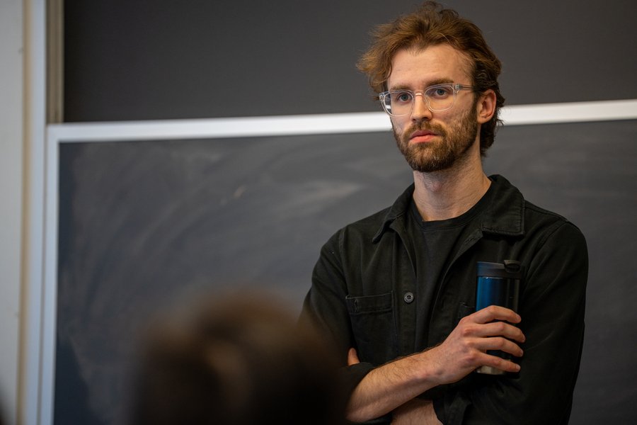 Close-up of MIchal Masny standing in front of a blackboard, holding an insulated beverage container