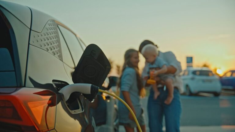 A mother with her baby boy and young daughter stands near an electric car charging station in a parking lot during a serene sunset, highlighting sustainable transportation and family connection.