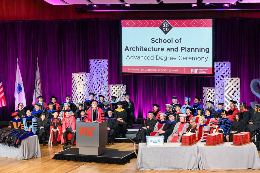 Wide view of the Kresge Auditorium stage shows faculty in graduation regalia seated behind a podium as Hashim Sarkis addresses graduates.