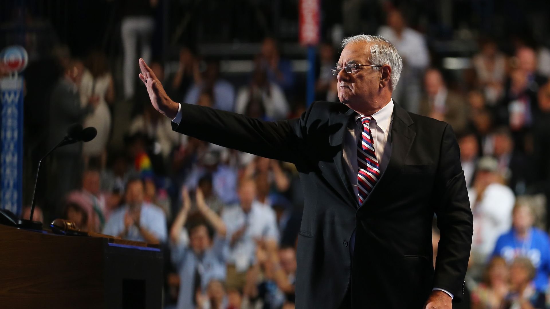 Barney Frank — wearing a dark suit with a red, white and blue striped tie — waves to a crowd on a stage at the Democratic National Convention.