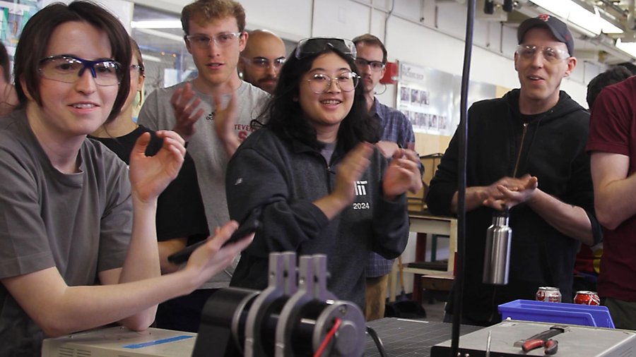 About a dozen MIT students cheering after a competitive moment in class