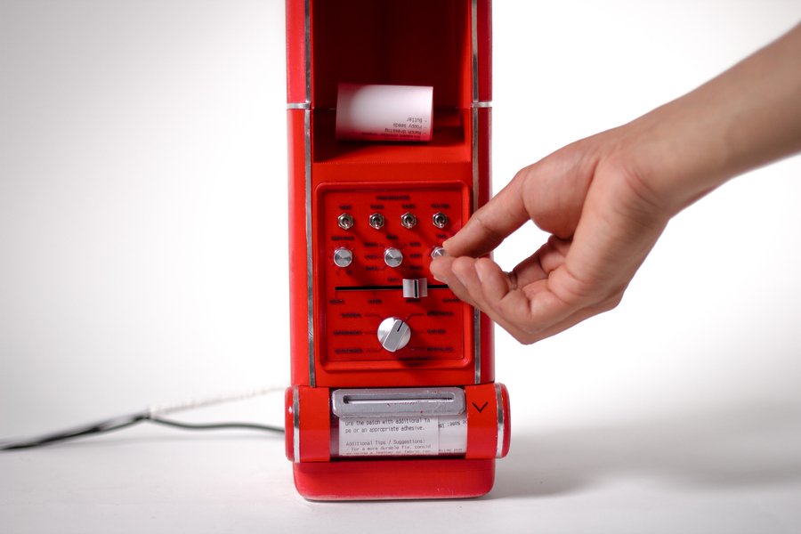 A hand turns a dial on the red Kitchen Cosmo device, about the size of a drip coffeemaker