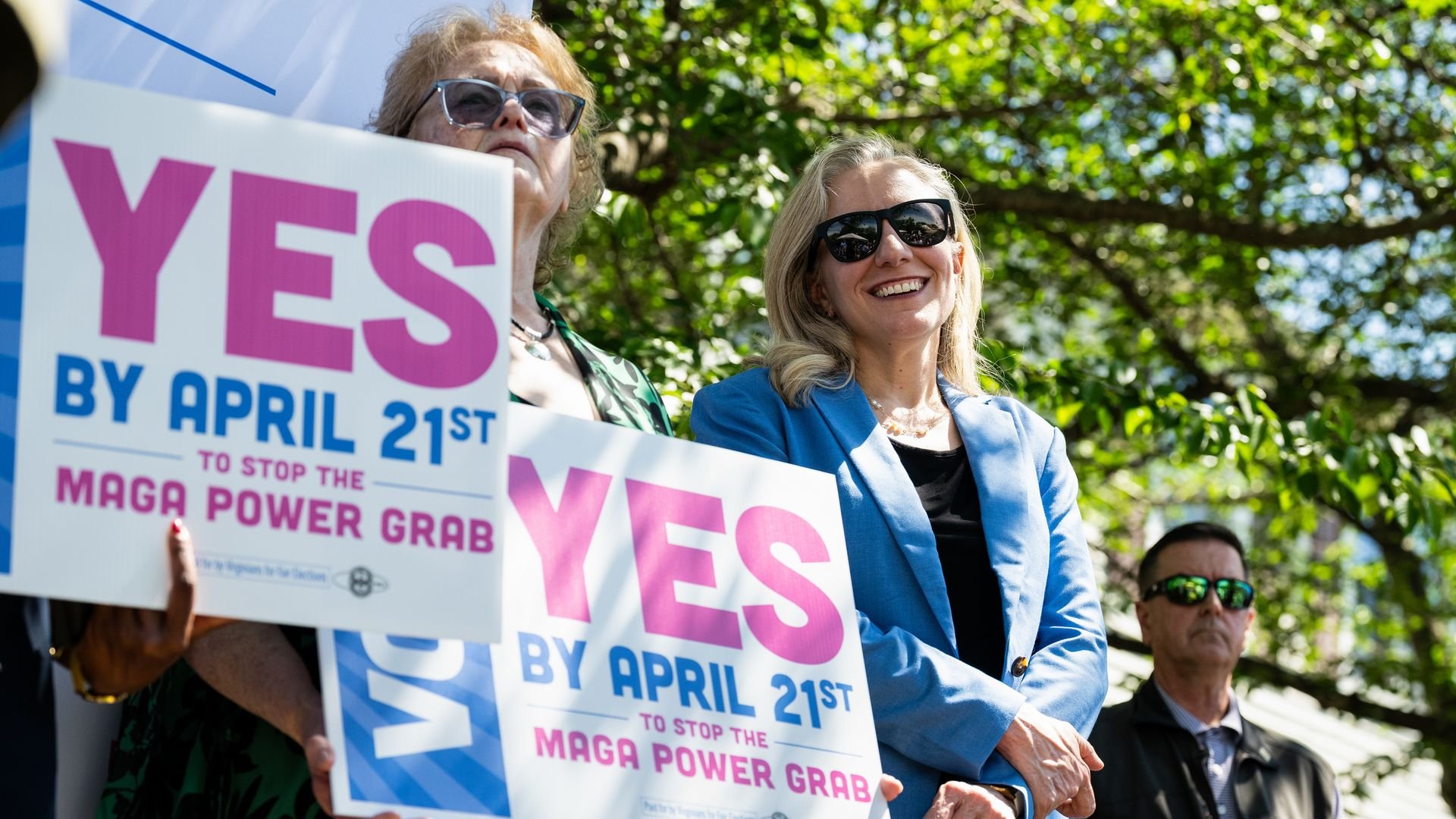 Virginia Gov. Abigail Spanberger, a a blue jacket, is shown with signs that say 