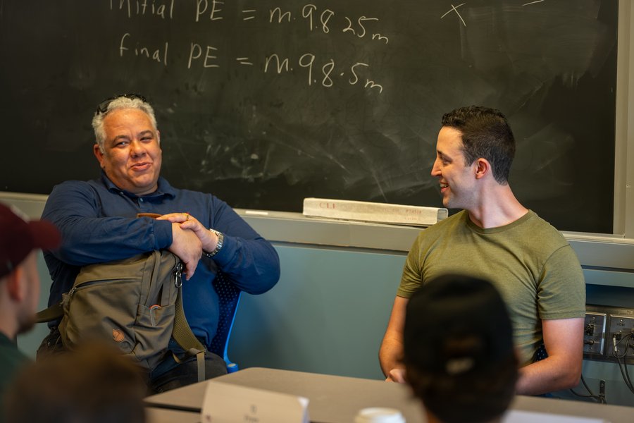 Nelson Olivieri and Justin Cole sit in front of a blackboard, presenting an admissions session