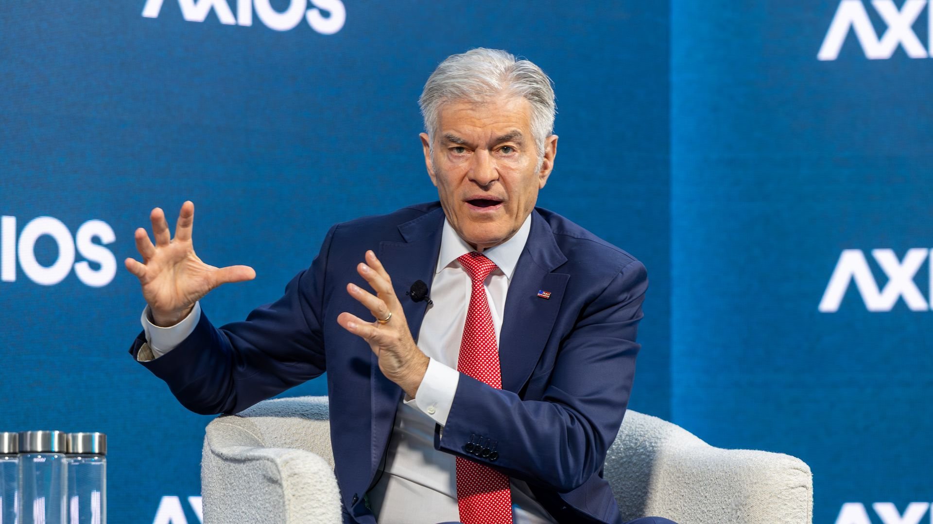 Gray-haired man in a navy suit and red tie speaks, using animated hand gestures while seated against a blue Axios backdrop.