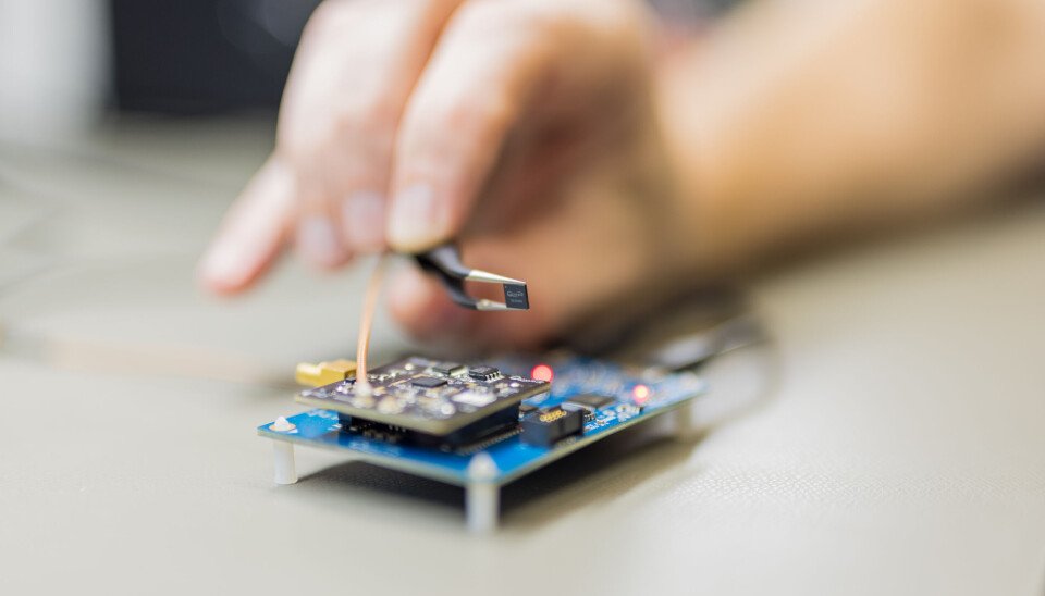 Qualinx QLX3xx chip held in tweezers above a circuit board