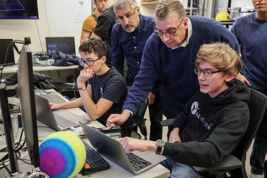 Nicholas Roy and Jonathan How look over a laptop together with students in a technology lab 