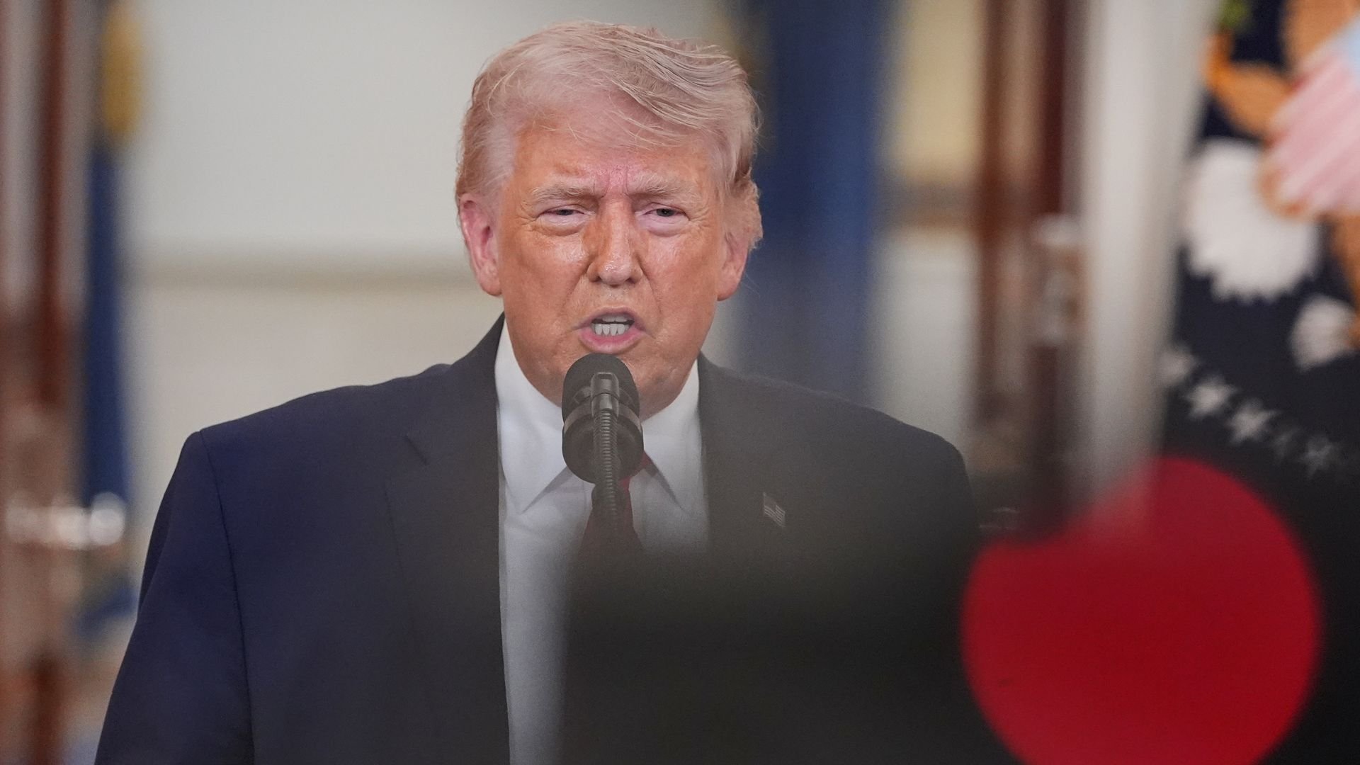 President Donald Trump speaks into a microphone during a televised address inside the White House.