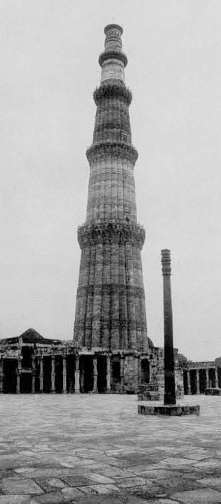 A massive metal pillar rising above stone ruiins, conical in shape with multiple segments.