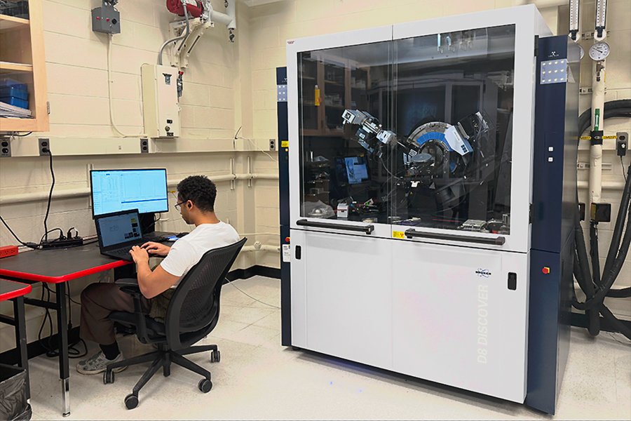 A person sits at a computer with a large x-ray diffractometer next to them.