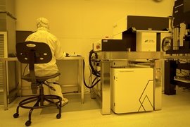 Yellow-tinted photo of a researcher in a clean suit using a large piece of lab equipment