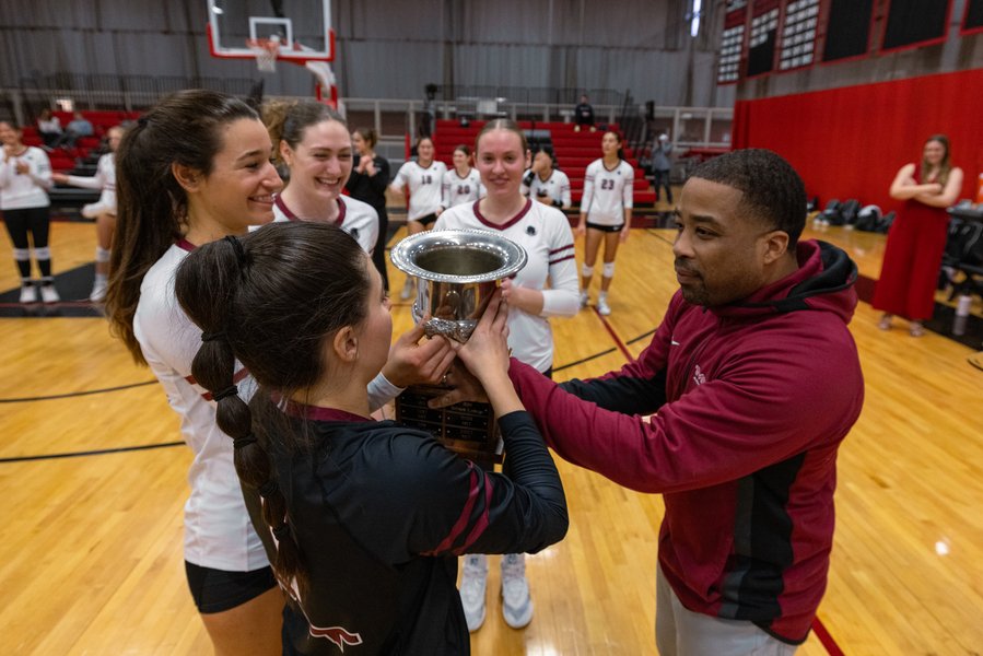 G. Anthony Grant presents a silver cup to four members of the MIT women's volleyball team.