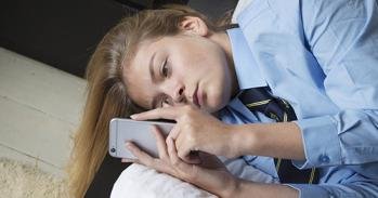 Teenager on a mobile phone, laying on a bed.