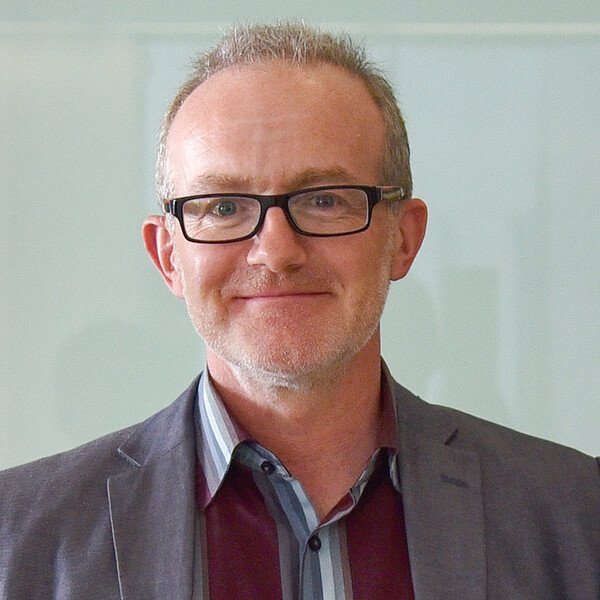 Smiling man with glasses, wearing a gray suit jacket and striped shirt.
