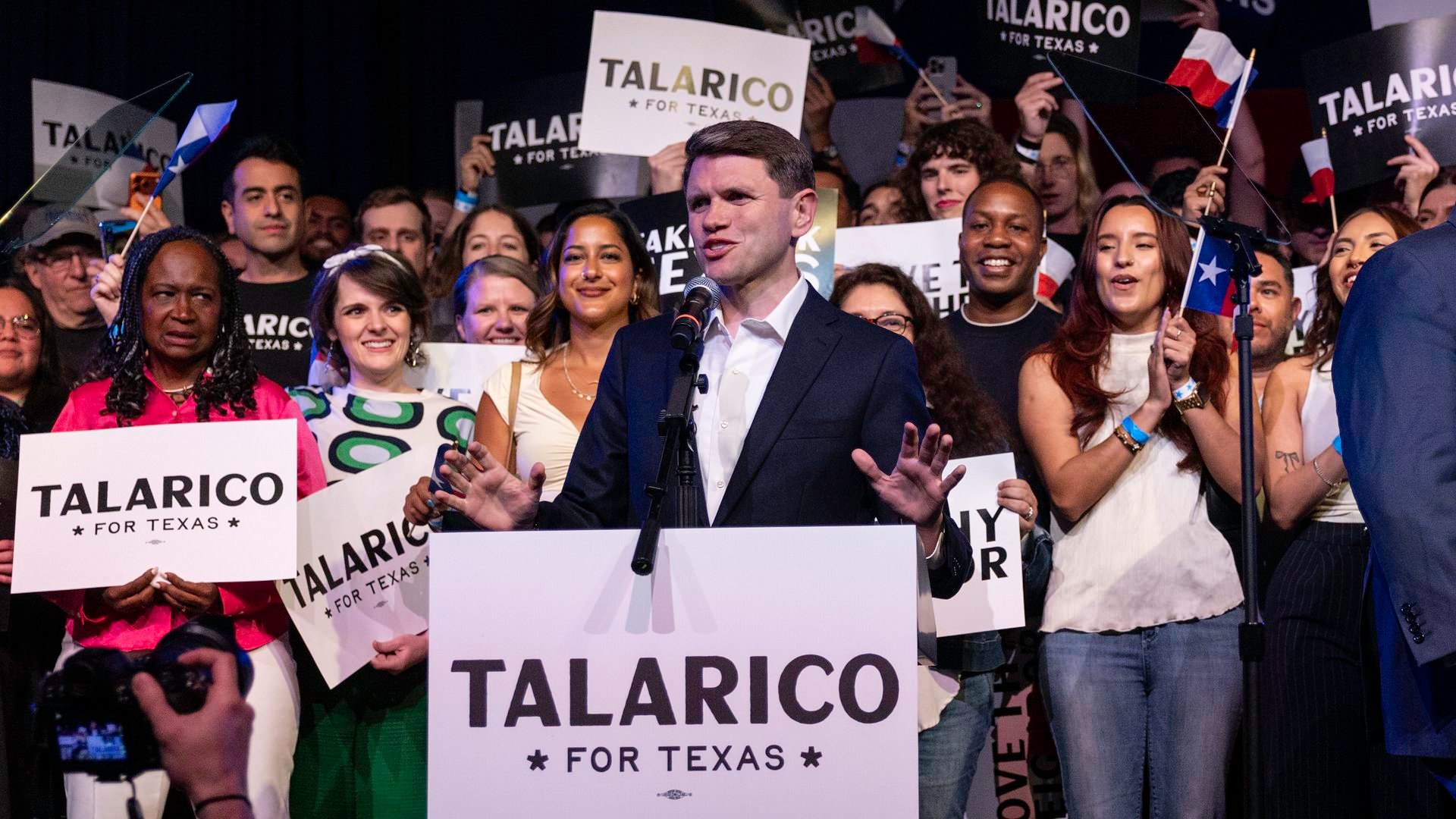 James Talarico stands behind a podium with his name on it, addressing supporters.