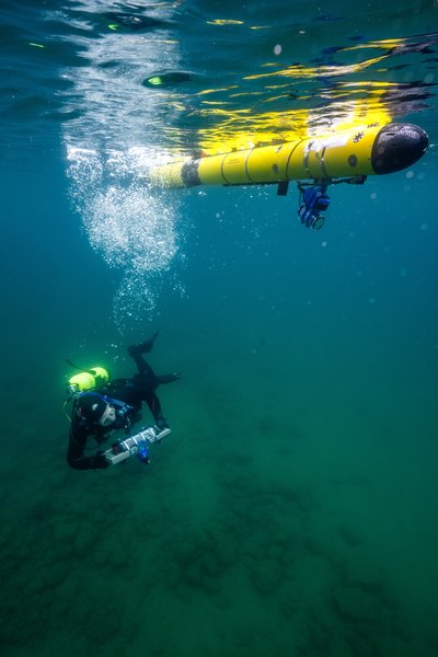A diver and autonomous underwater vehicle swim together underwater. 