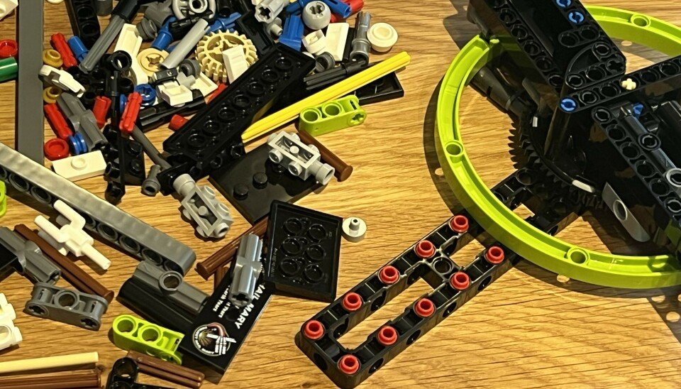A pile of LEGO Technic pieces and a partly built black structure on a wooden tabletop.