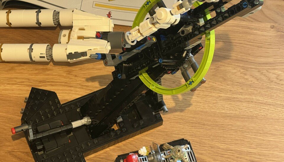 LEGO Technic spacecraft model on a stand with two minifigures on a wooden surface.