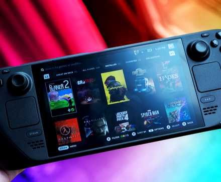 A Steam Deck on a colorful background held in one hand.