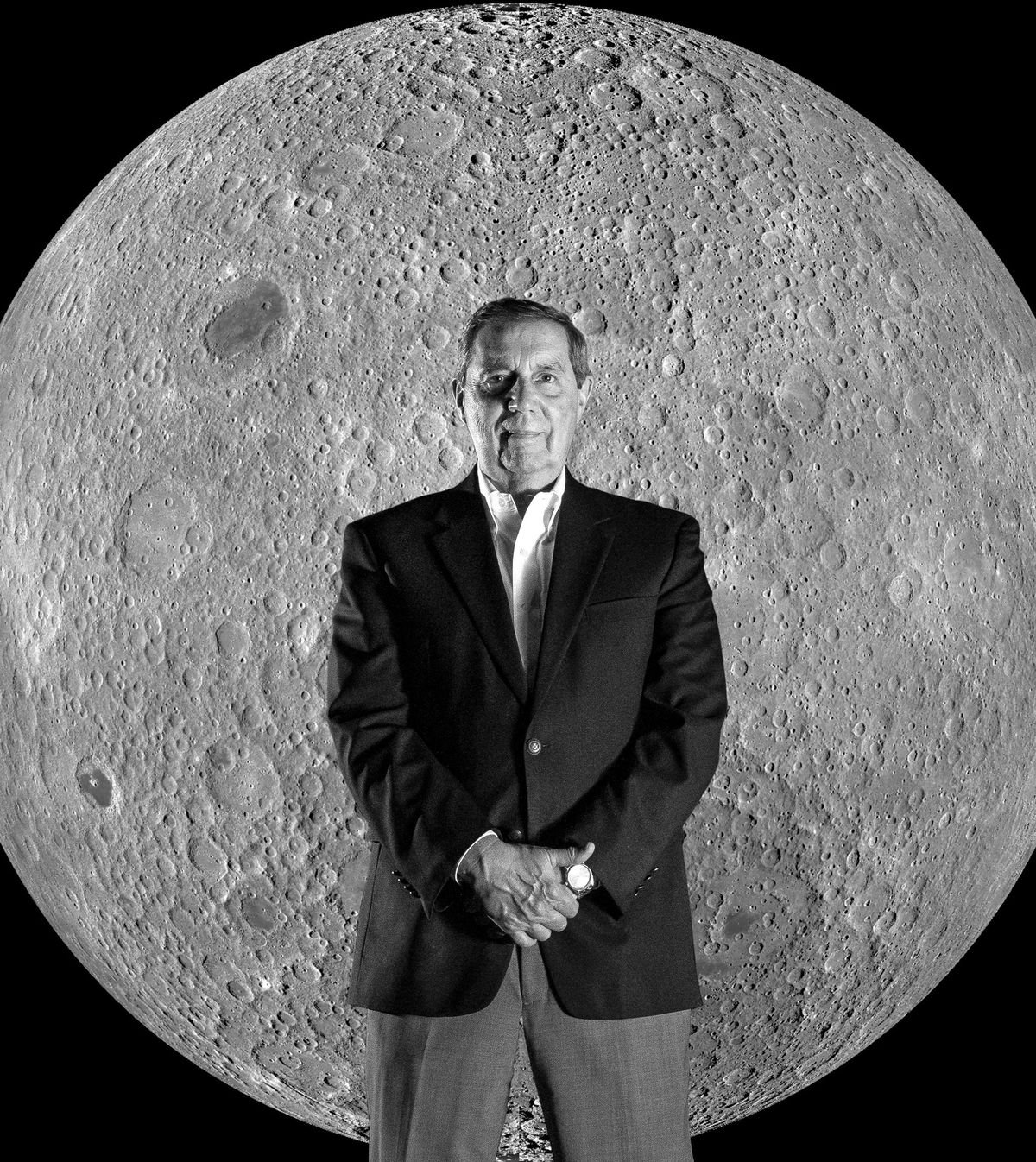 Photo of a man in a sports jacket standing in front of a detailed image of the moon. 