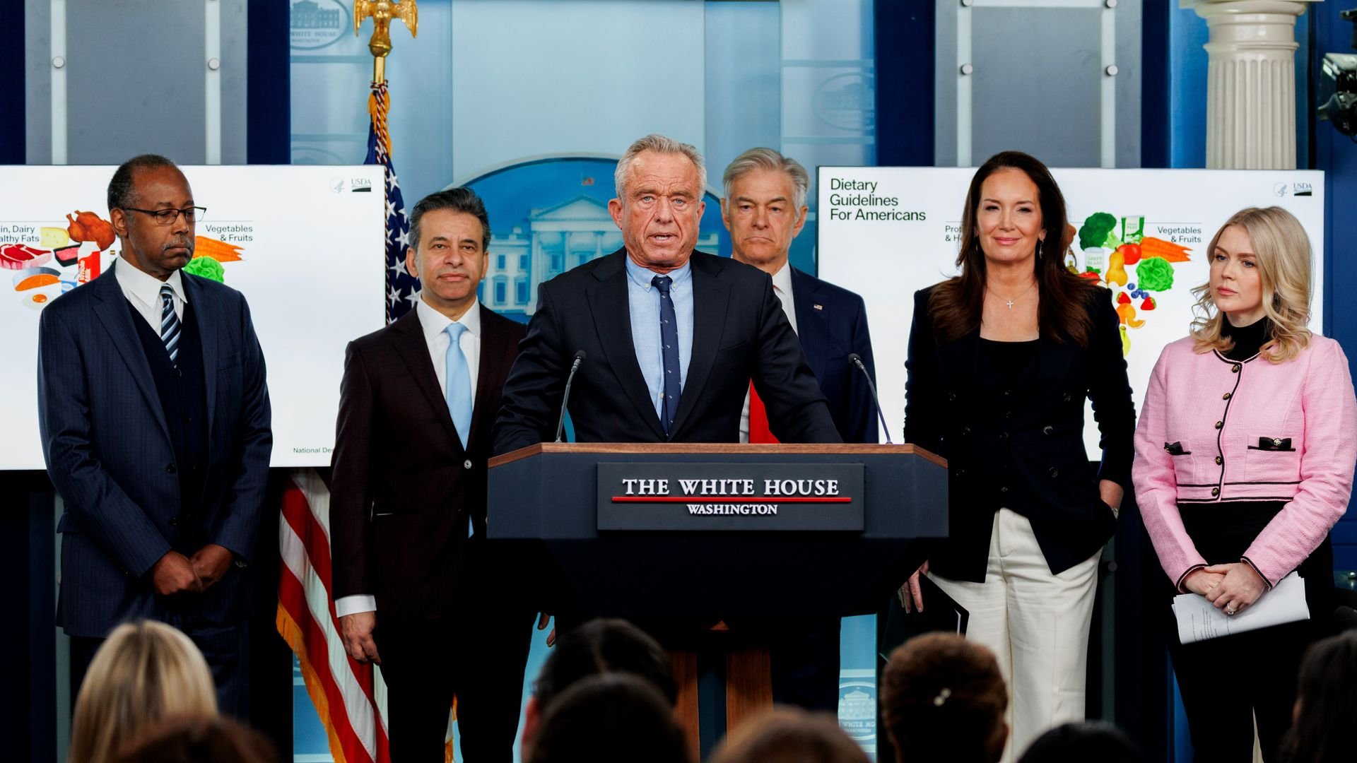 Ben Carson, Marty Makary, Robert F. Kennedy Jr, Mehmet Oz, Brooke Rollins and Karoline Leavitt stand behind a podium. 