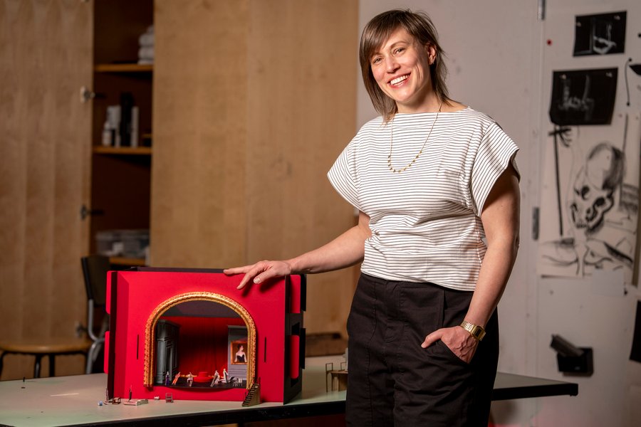 Sara Brown stands next to the stage model, which has a giant golden arch into a red room.