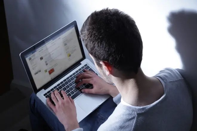 Young male sitting in the dark with his laptop, Ttweeting.