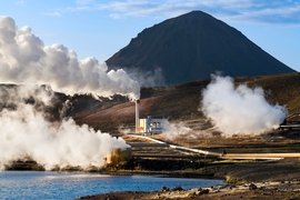 Photo of modest-sized power plant on treeless plain emiting steam clouds, with mountain in background