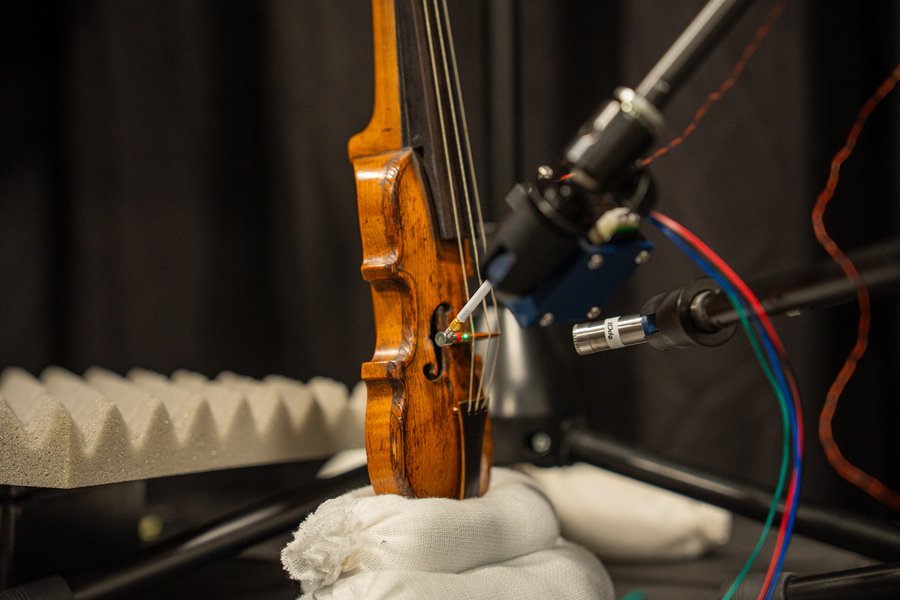 An antique violin is surrounded by a various technical equipment.