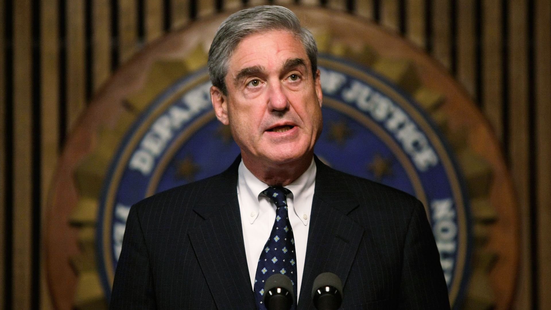 Robert Mueller standing in front of the FBI seal. 