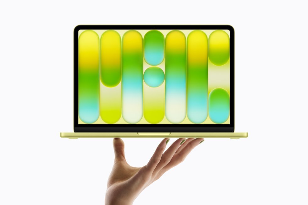 A hand holds up the all-new MacBook Neo in citrus.