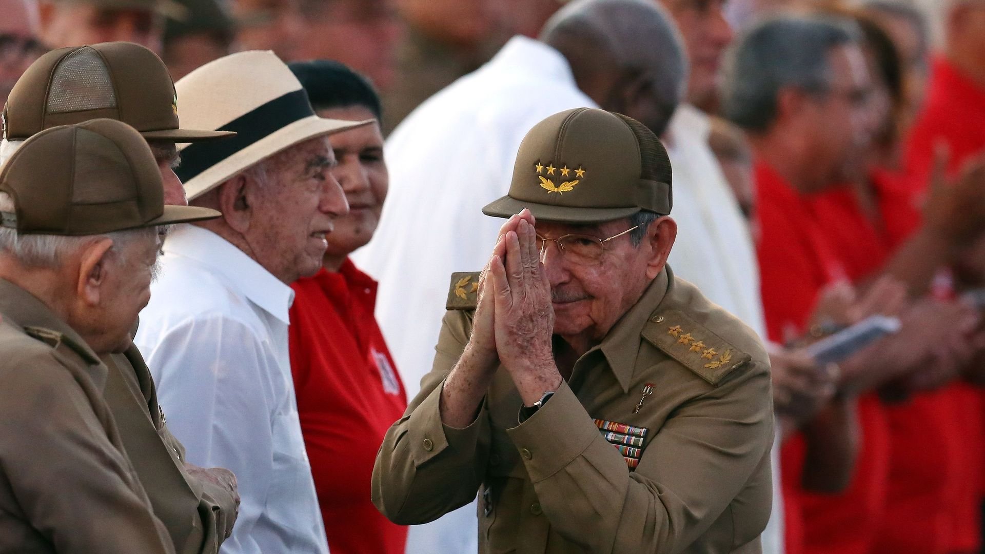Raul Castro makes a praying gesture in military uniform.