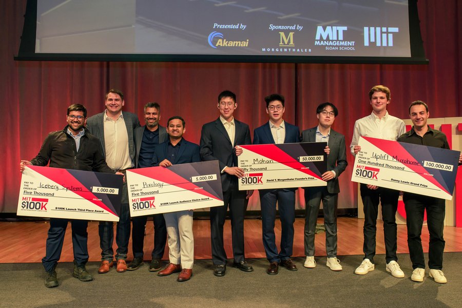 Four teams stand on stage, each with a giant check.