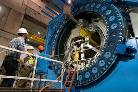 Three people inspect a gigantic blue Collider, with a circular opening.