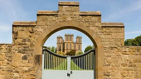 Alamy A stately home is seen through closed gates in a stone wall (Credit: Alamy)