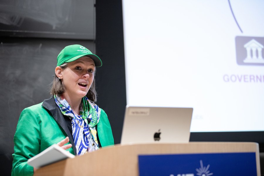 Georgina Campbell Flatter, wearing a bright green jacket and matching baseball cap, speaks at a lectern.