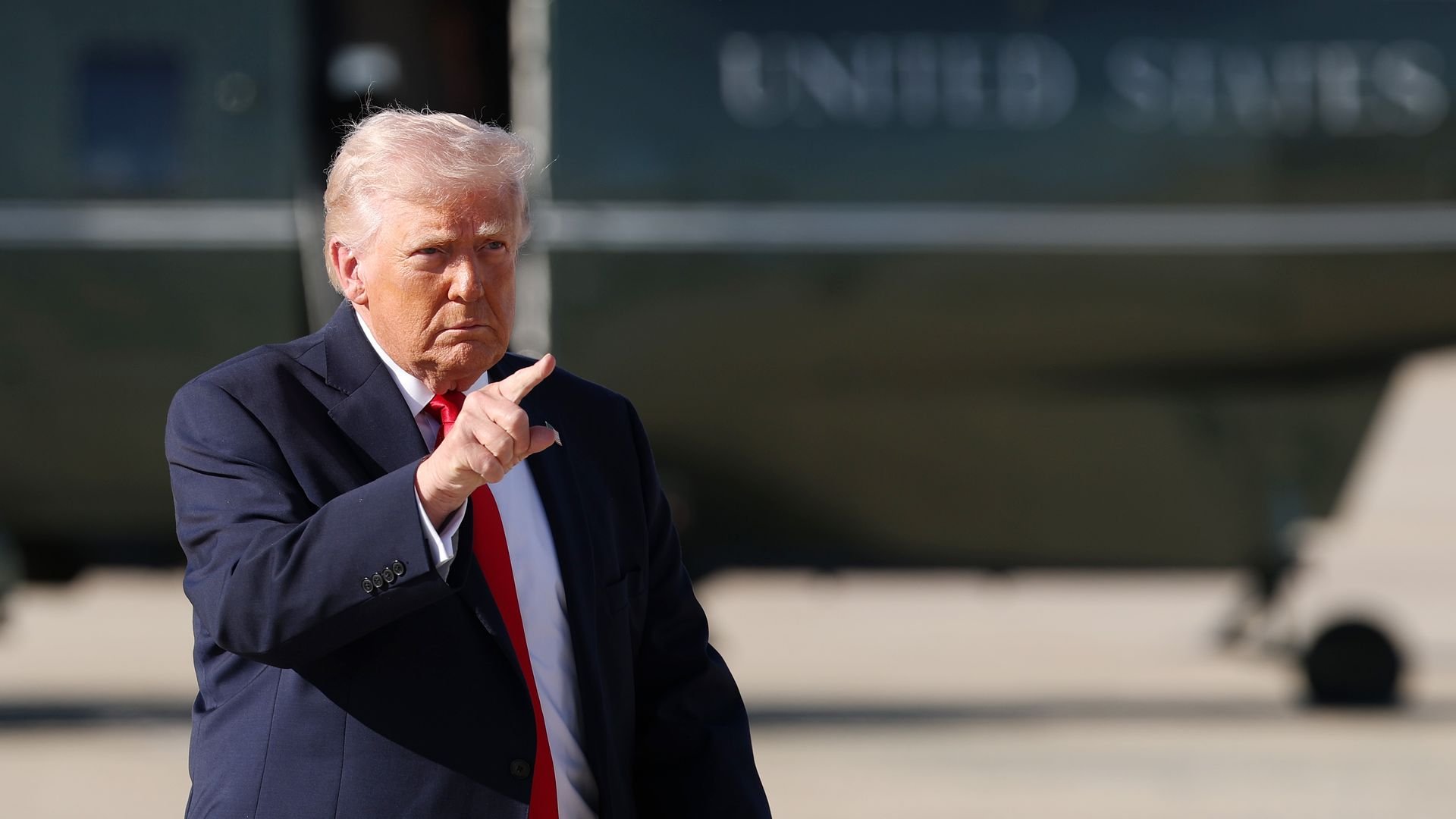 Donald Trump points with Marine One in the background.