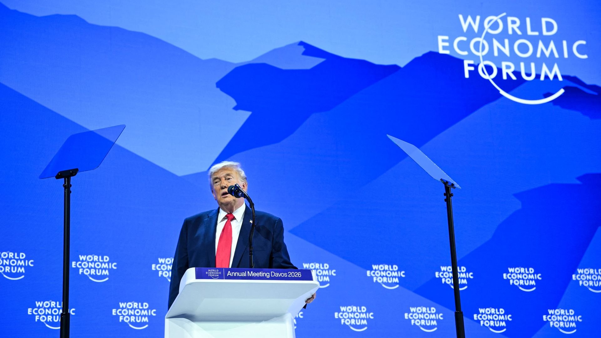 President Trump — wearing a dark suit, a white collared shirt and a red tie — speaks into a microphone from behind a white podium at the World Economic Forum.