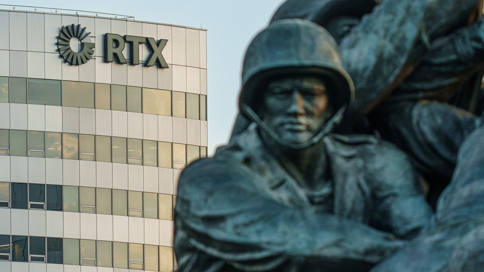 Close-up of a bronze soldier statue in front of a beige office building with windows and a large black 