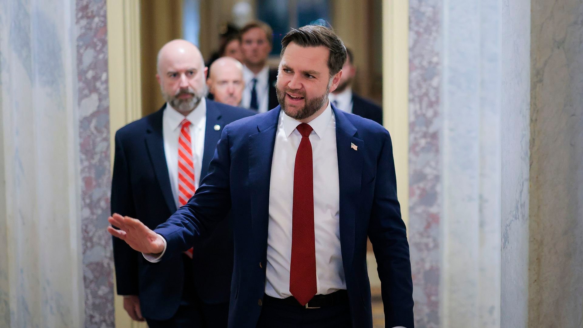 Vice President Vance walks down a hall, followed by another man.