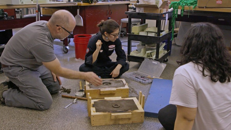 An instructor kneels on the floor with two students